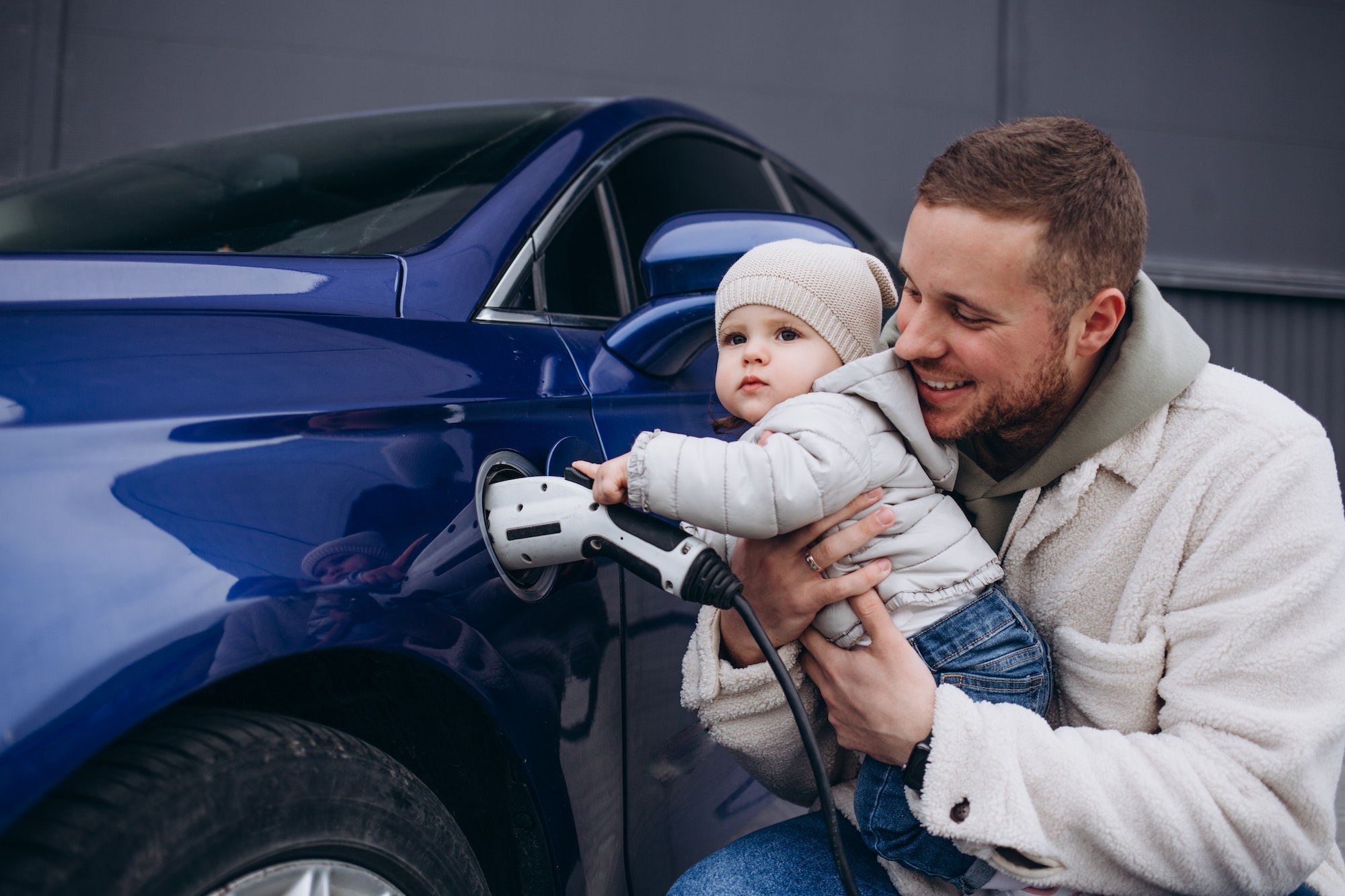 young father with daughter in his arms charging an electric car.